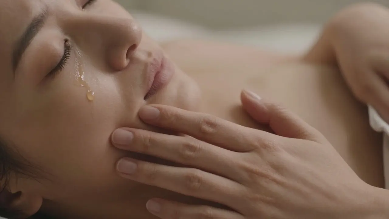 Ruka klidně leží na břiše, slzy na tváři, jedna kapka oleje kape pomalu — okamžik vnitřního uvolnění.